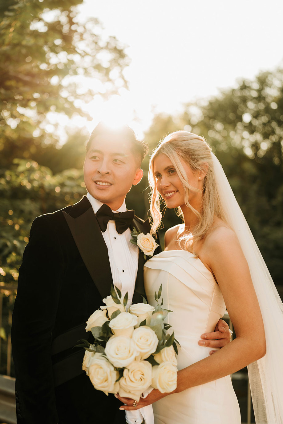 a bride with white rose bouquet and groom posing in soft golden sunlight