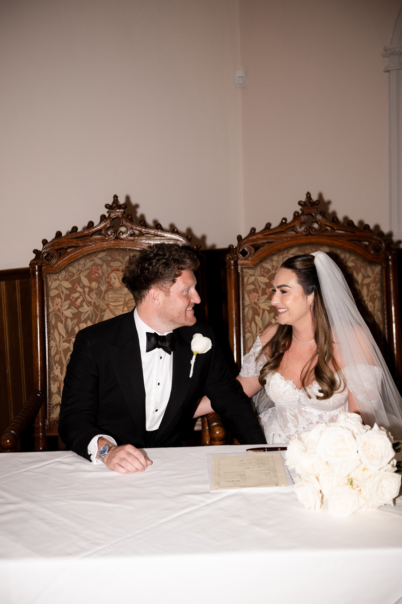 Bride and groom smiling together while signing the wedding register at Crossbasket Castle near Glasgow.