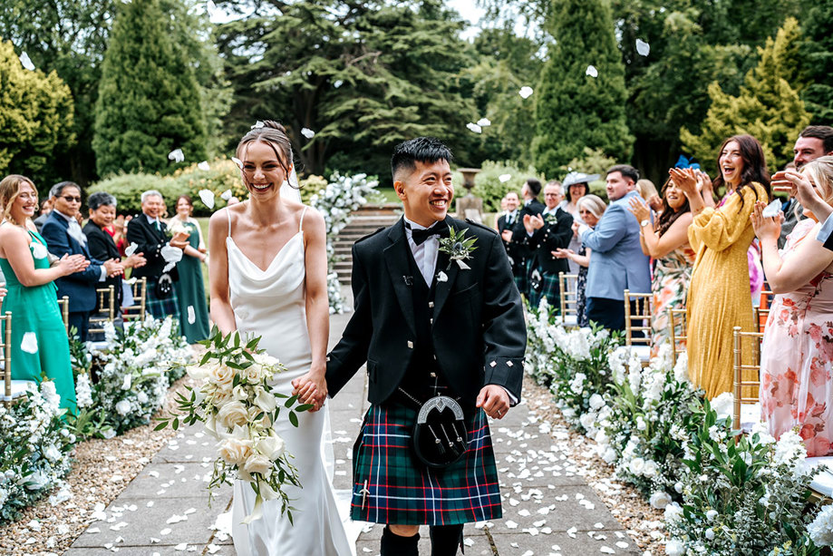 wedding guests throw white confetti over bride and groom after outdoor ceremony at mar hall