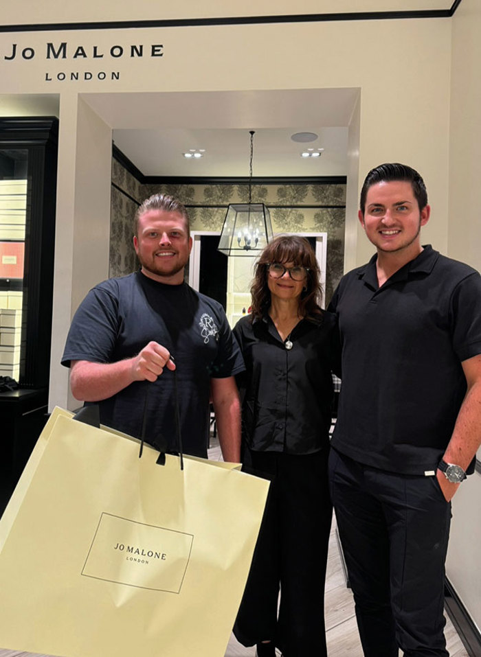 two men standing with a woman in a Jo Malone London shop. One man is holding a large Jo Malone London shopping bag