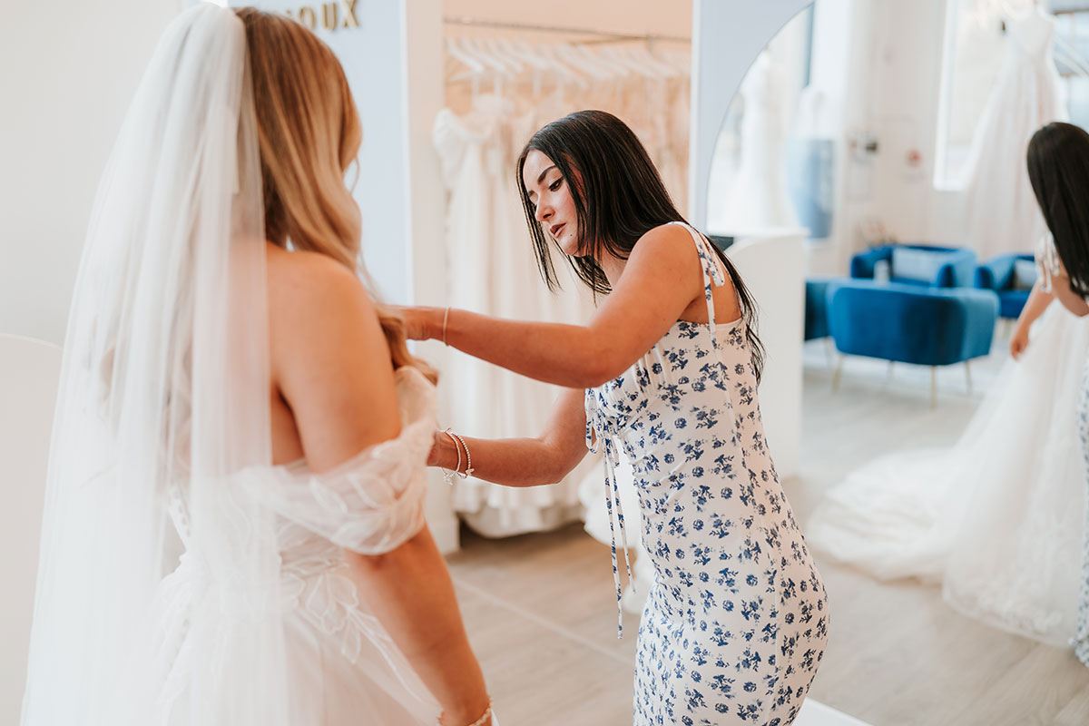 Bridal consultant adjusting off-the-shoulder wedding dress with veil at Bijoux Bridal