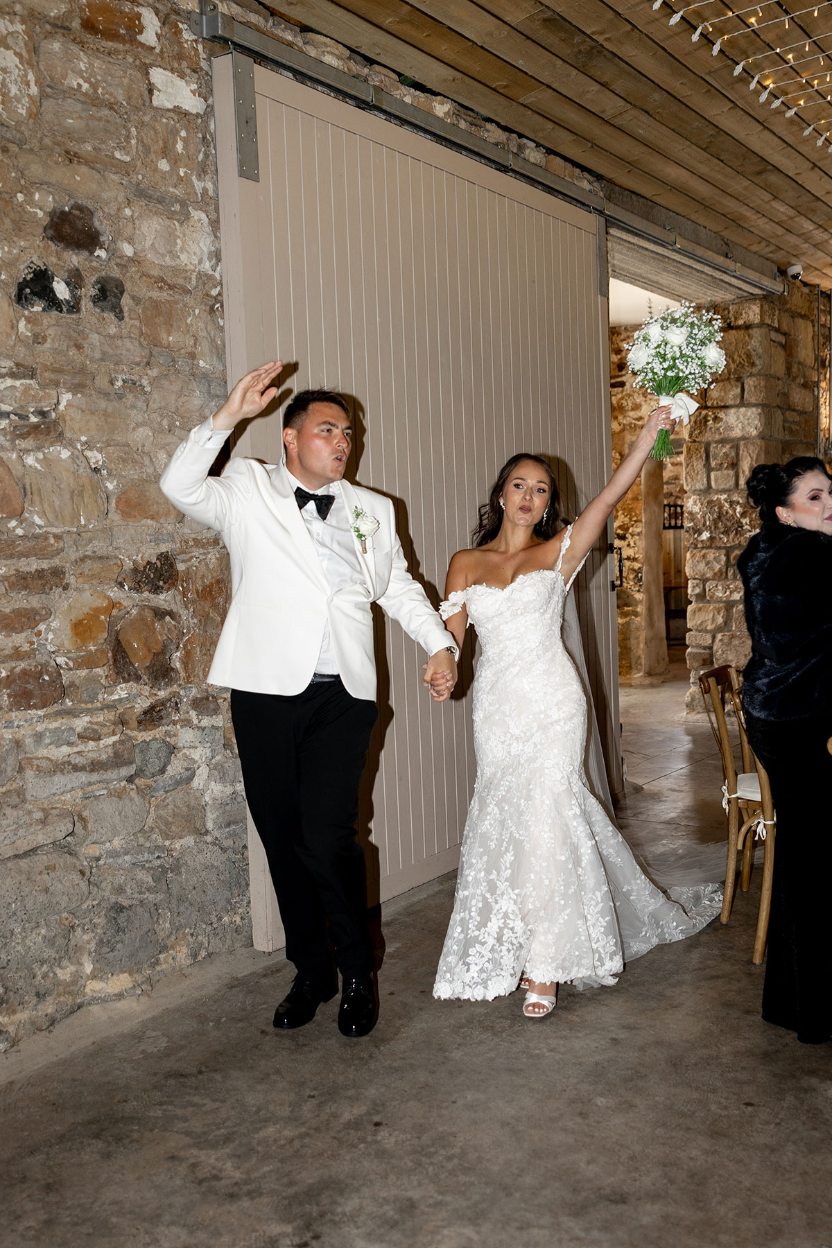 Bride and groom make a joyful entrance to their Falside Mill wedding reception, holding hands and celebrating with guests inside the rustic stone venue.