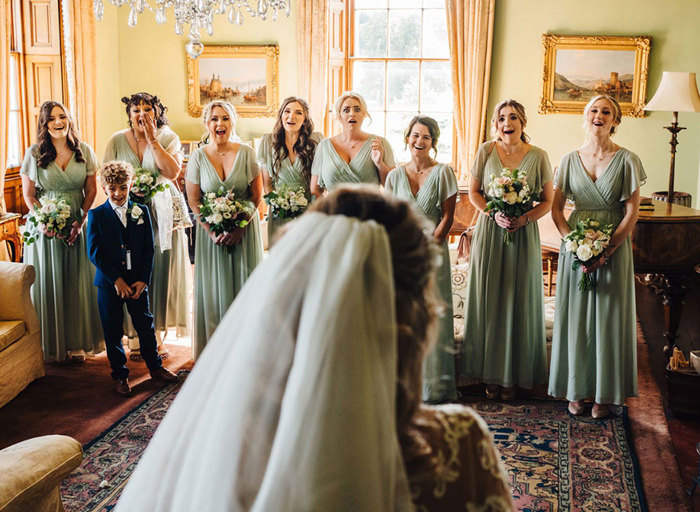 Bridesmaids' faces of excitement and emotion as they see bride in her dress for the first time