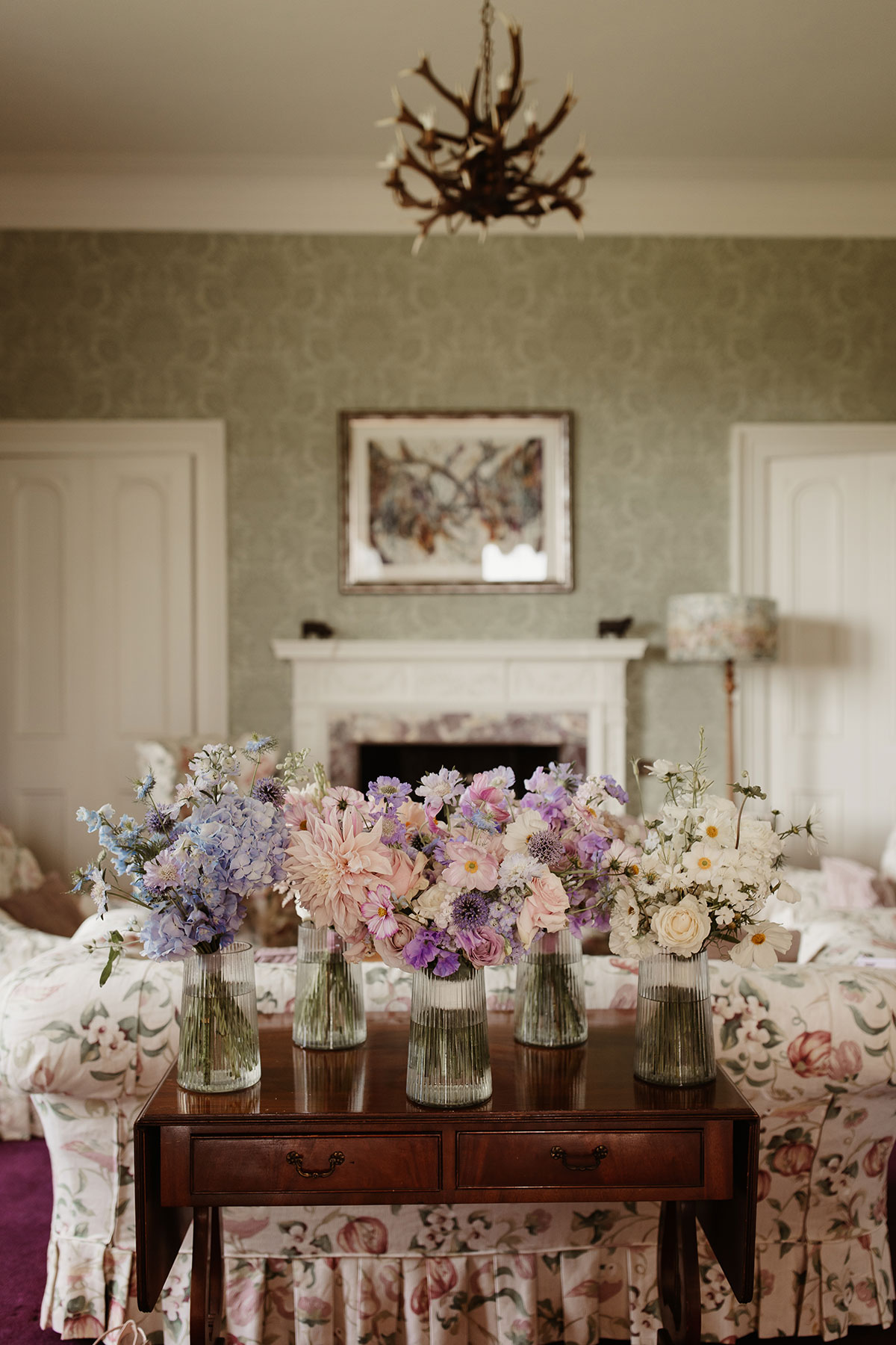 pastel wedding flowers in glass jars sitting on a wooden table in a pale green room at Netherdale House