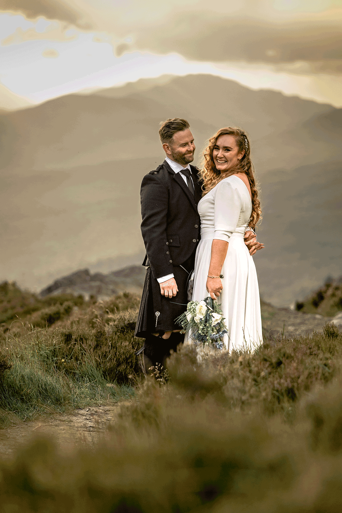 Bride and groom embrace after their Scottish mountain elopement with soft golden-hour light across the landscape