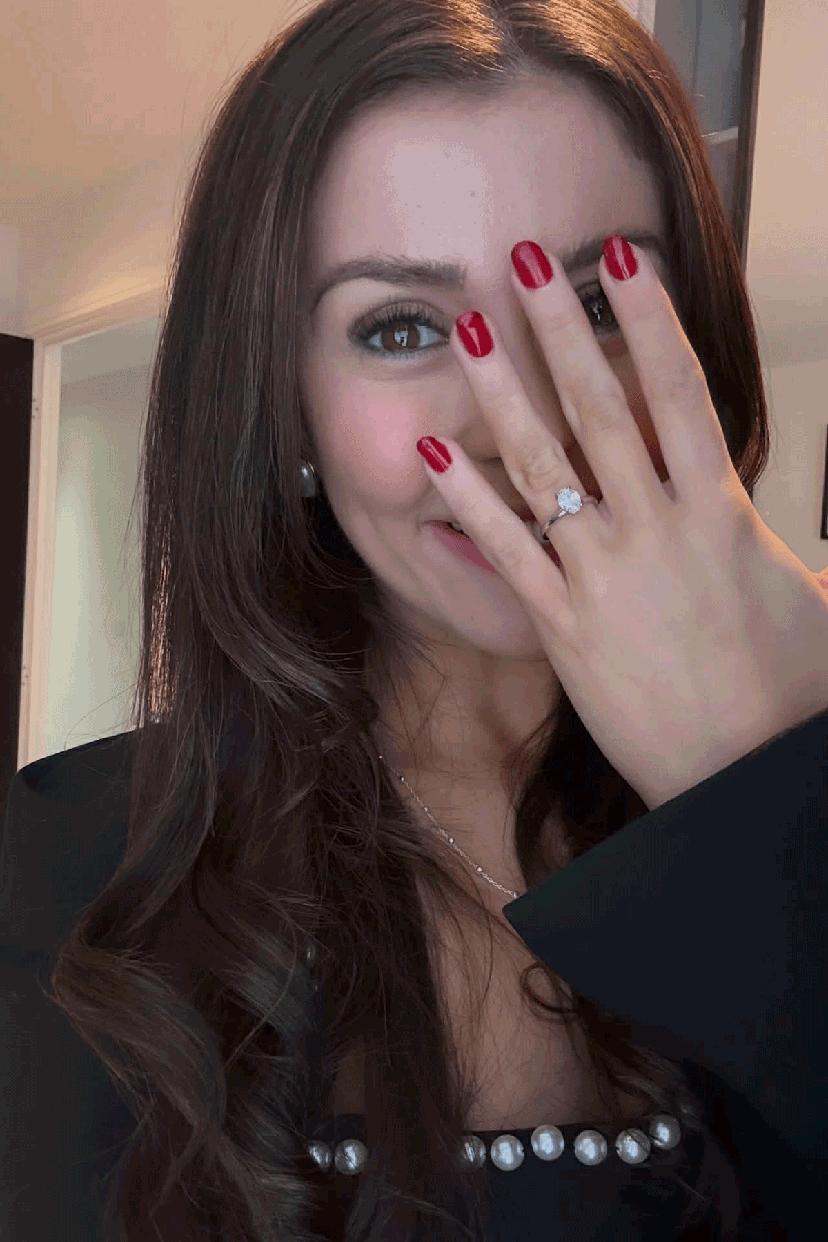 Bride-to-be smiling while showing diamond engagement ring on left hand indoors