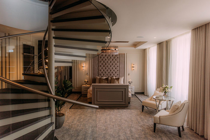 a spiral staircase going up past a large bed and lounge seating
