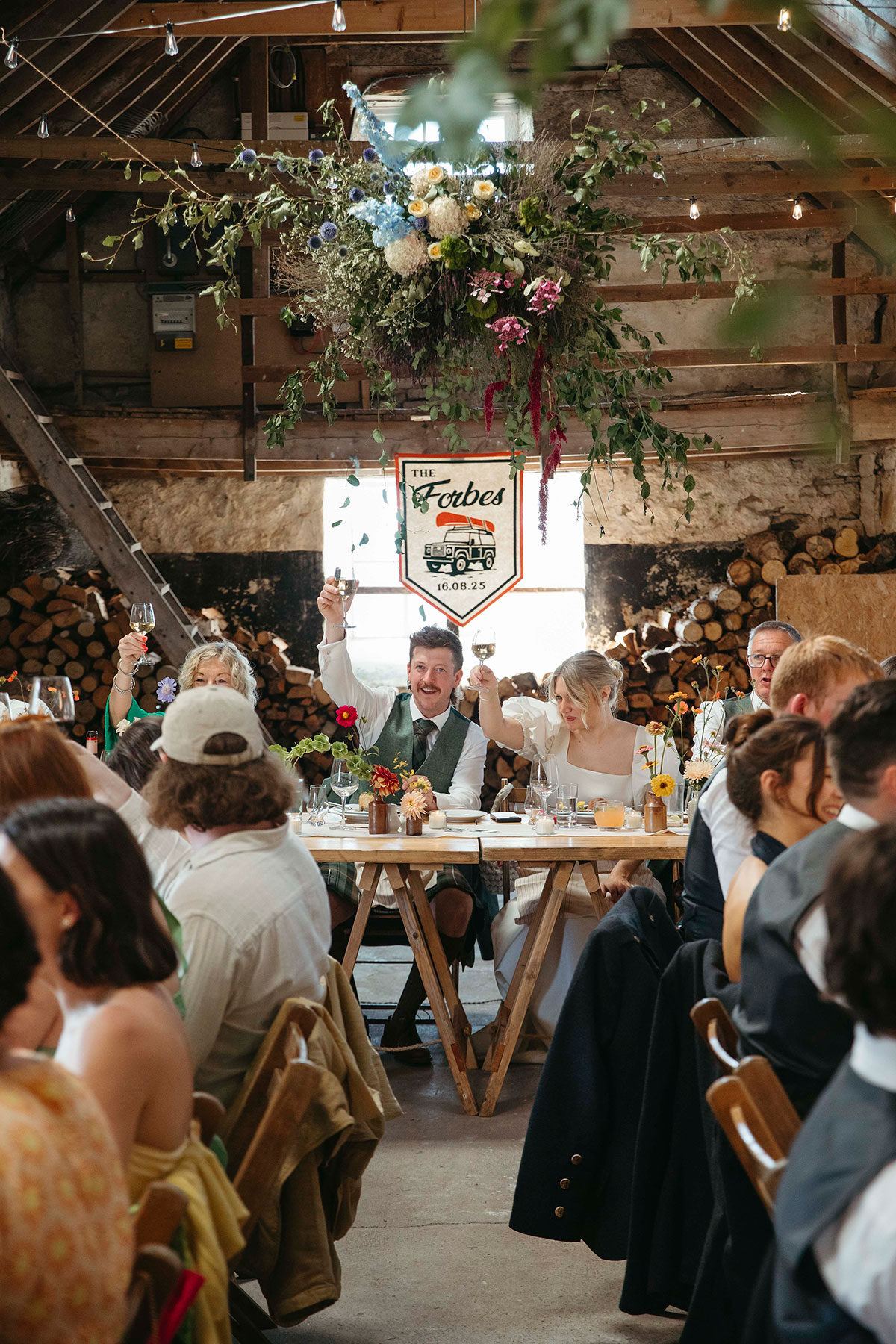 Bride and groom raise glasses during rustic barn wedding reception in the Cairngorms Highlands