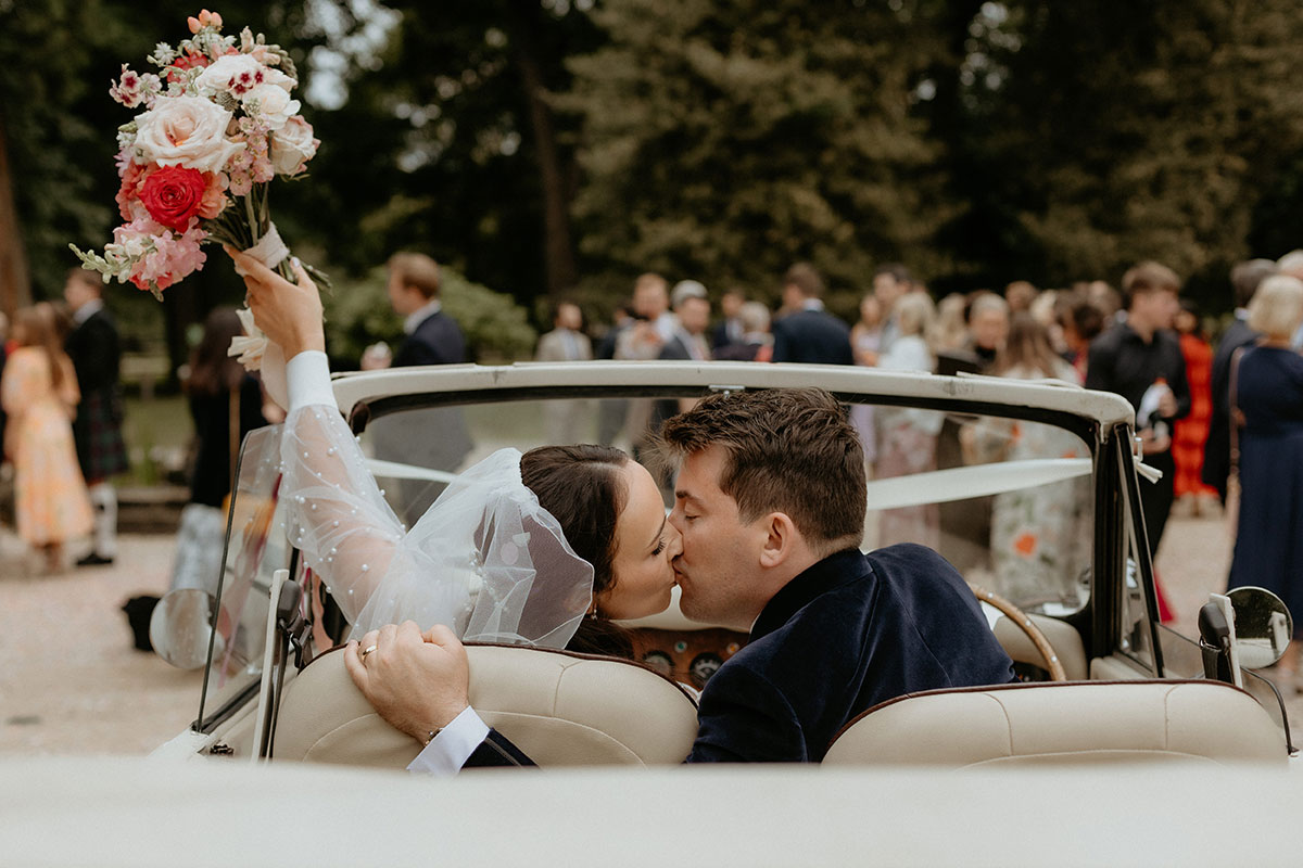a bride and groom kissing in a convertible car with its top down