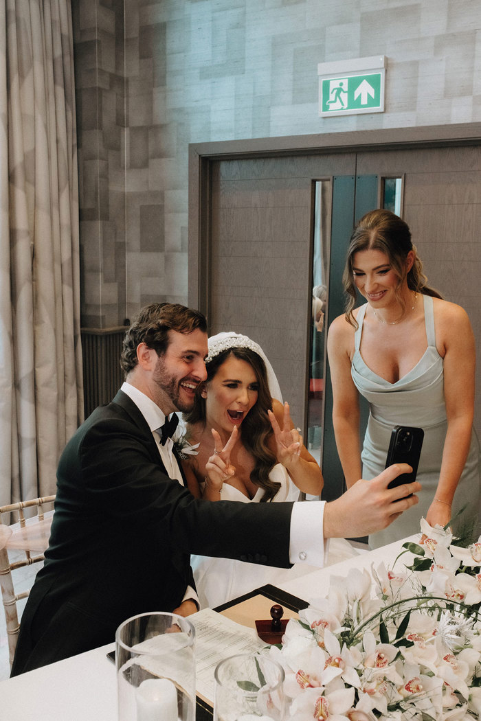 a bride and groom pose for a selfie while seated at a table decorated with white orchids