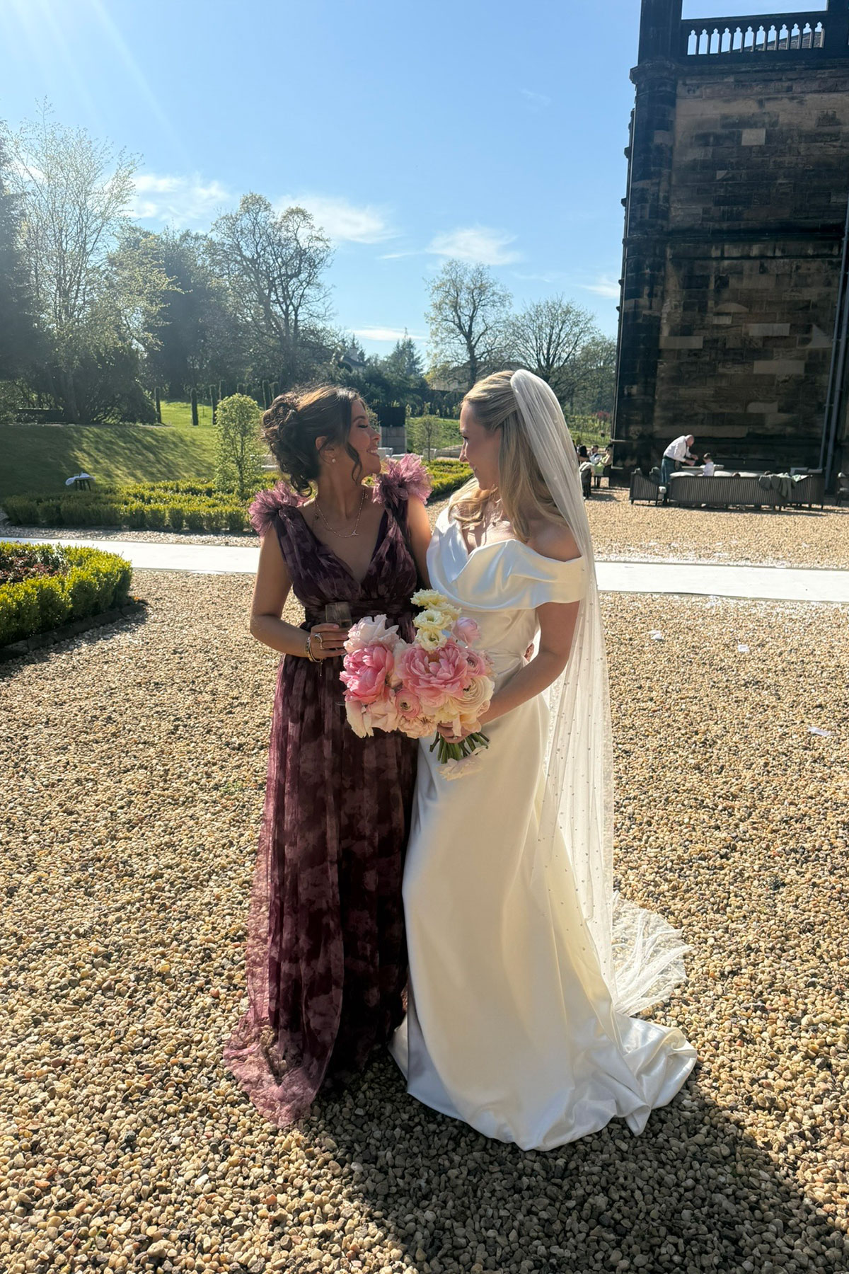 Bride and wedding guest sharing a smile outside a Scottish castle wedding venue with spring sunshine and formal gardens