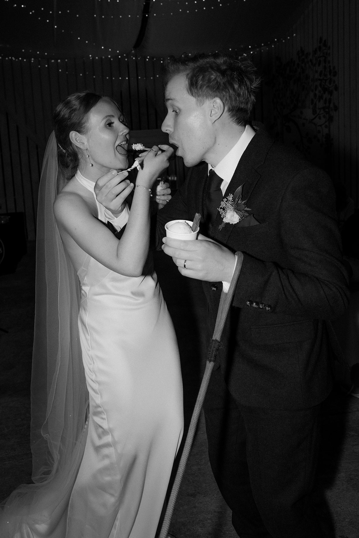 Black and white photo of bride and groom feeding each other dessert during evening reception