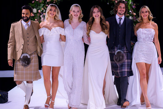 Group of men in kilts and women in wedding dresses standing next to each other 