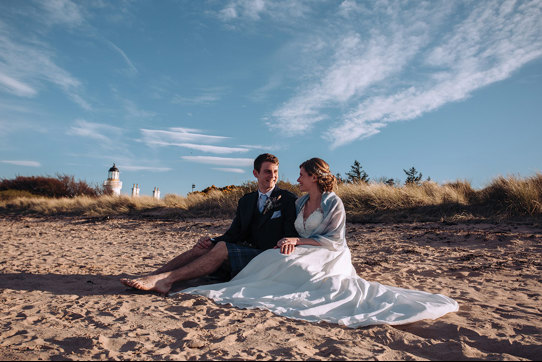 Bride and groom sitting on beach smiling at each other