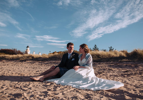 Bride and groom sitting on beach smiling at each other