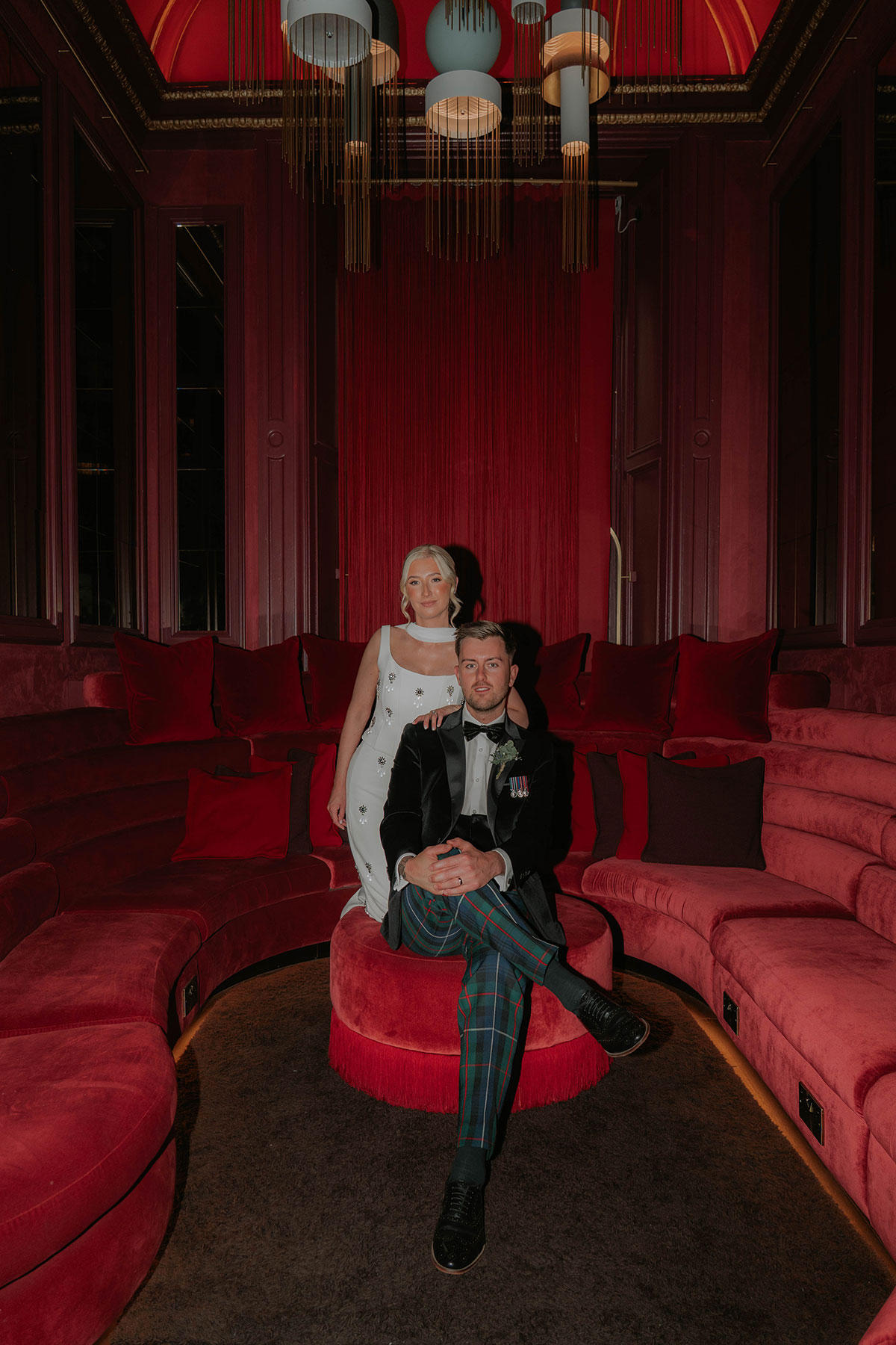 Bride and groom posing in a dramatic red velvet lounge during their stylish Edinburgh city wedding