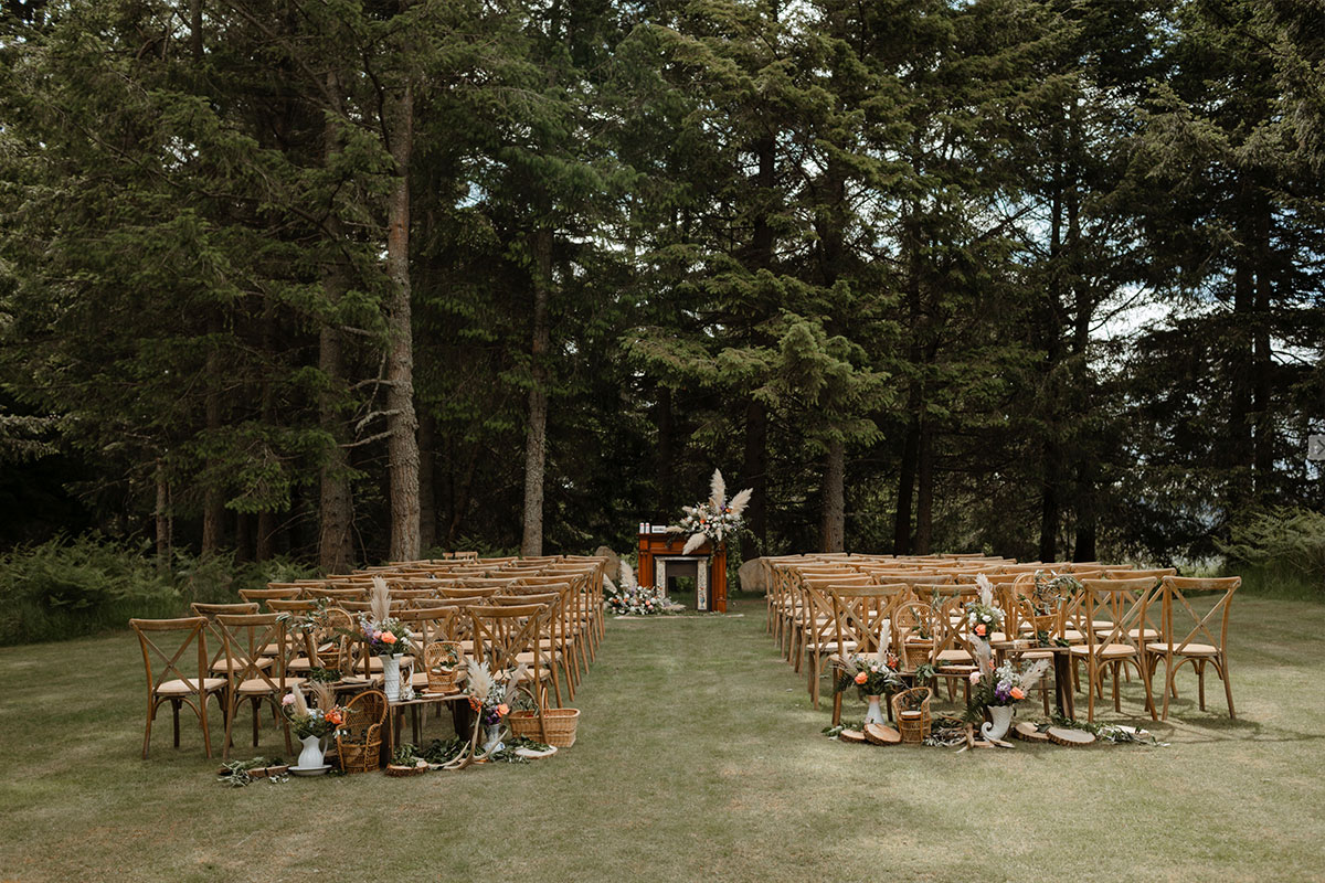 A wedding ceremony set up next to a woodland with wooden chairs and an arch