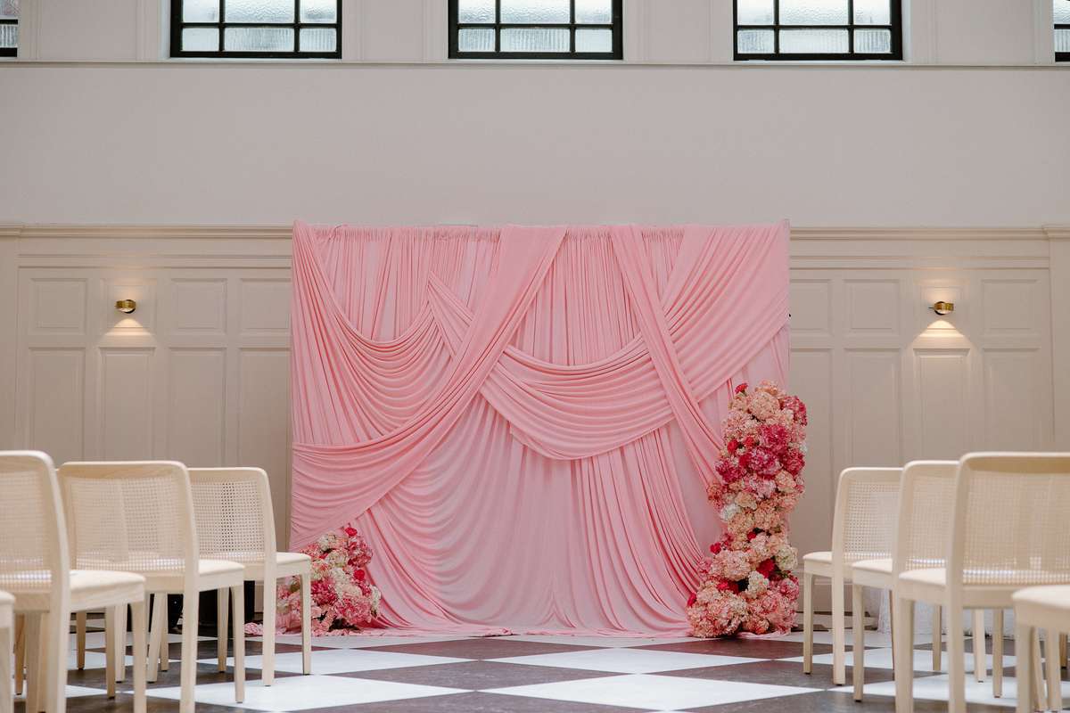 Wedding ceremony setup at The Collector’s Hall Glasgow featuring a pink draped backdrop, colourful flowers and chequerboard floor.