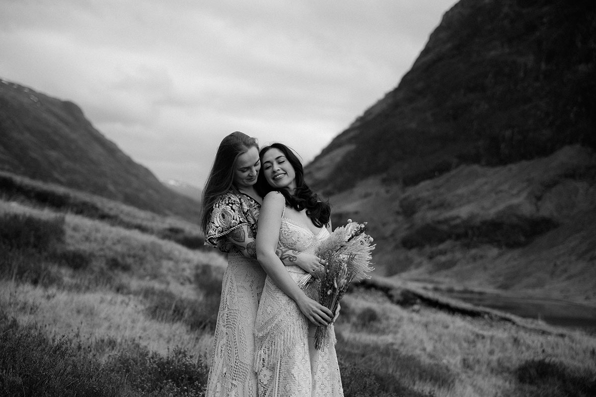 Black and white portrait of a couple embracing during a Glencoe elopement shoot, with the Scottish Highlands in the background.