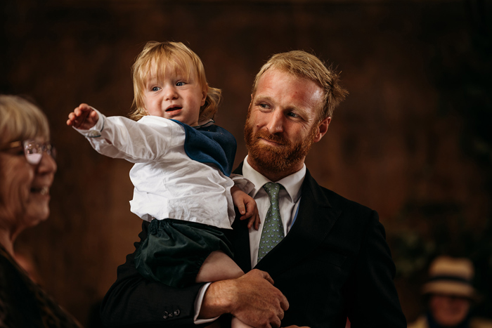 A Person Wearing A Tie Carrying A Young Child
