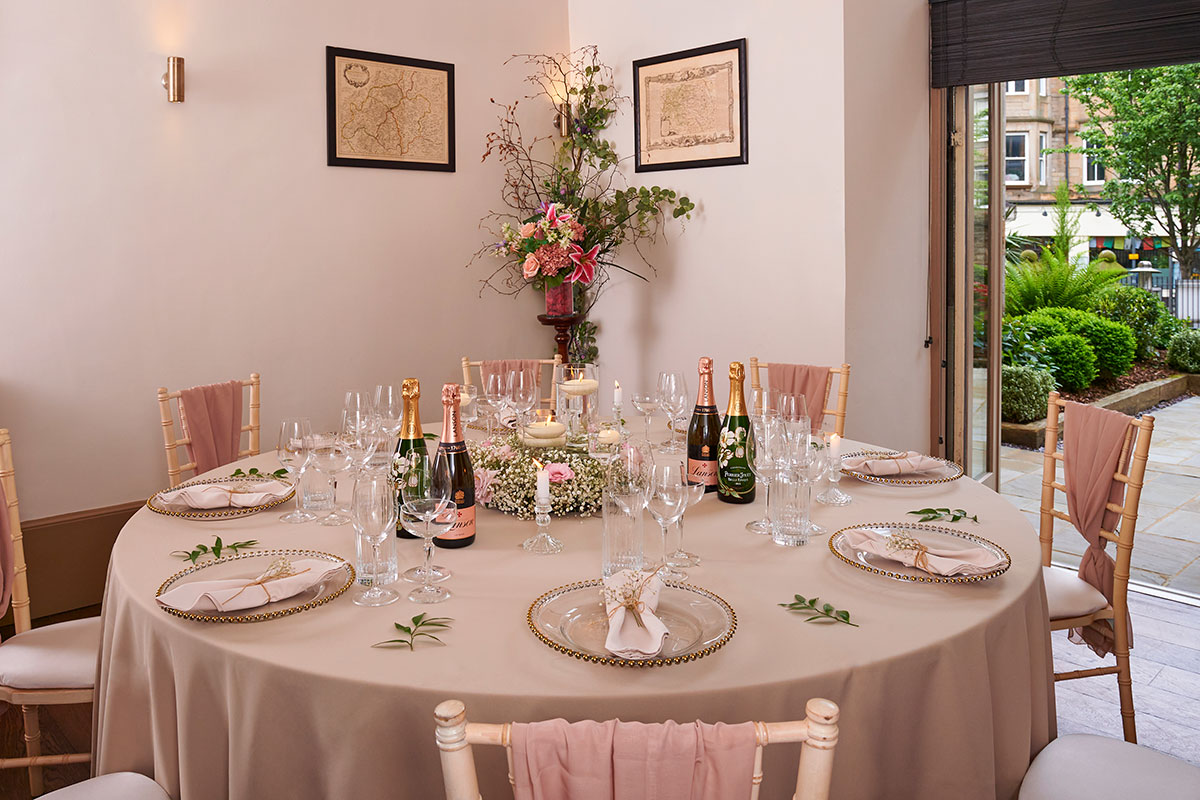 Round wedding table styled with blush linens, florals and champagne bottles in an intimate reception space