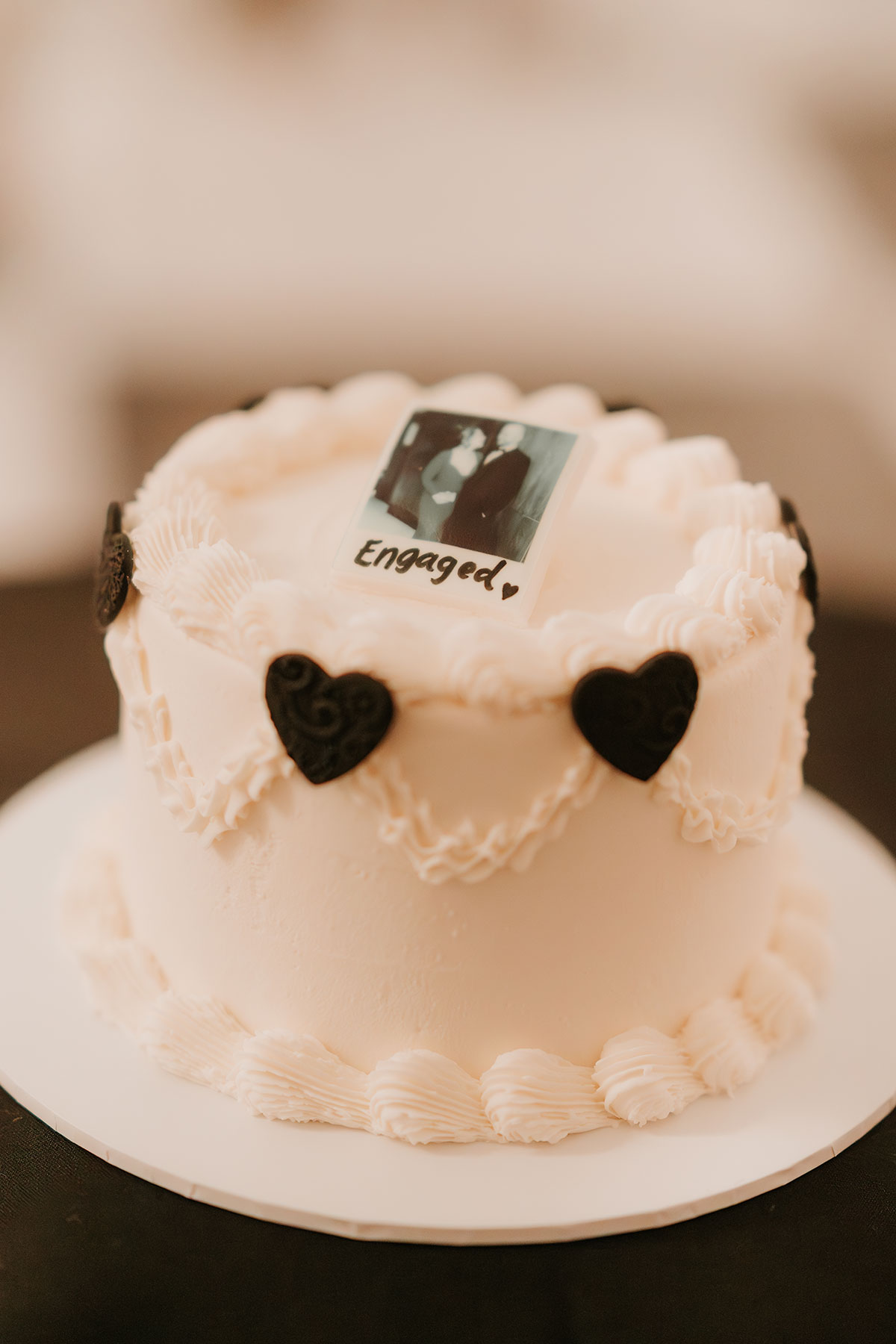 White vintage engagement cake with black heart details and Polaroid topper