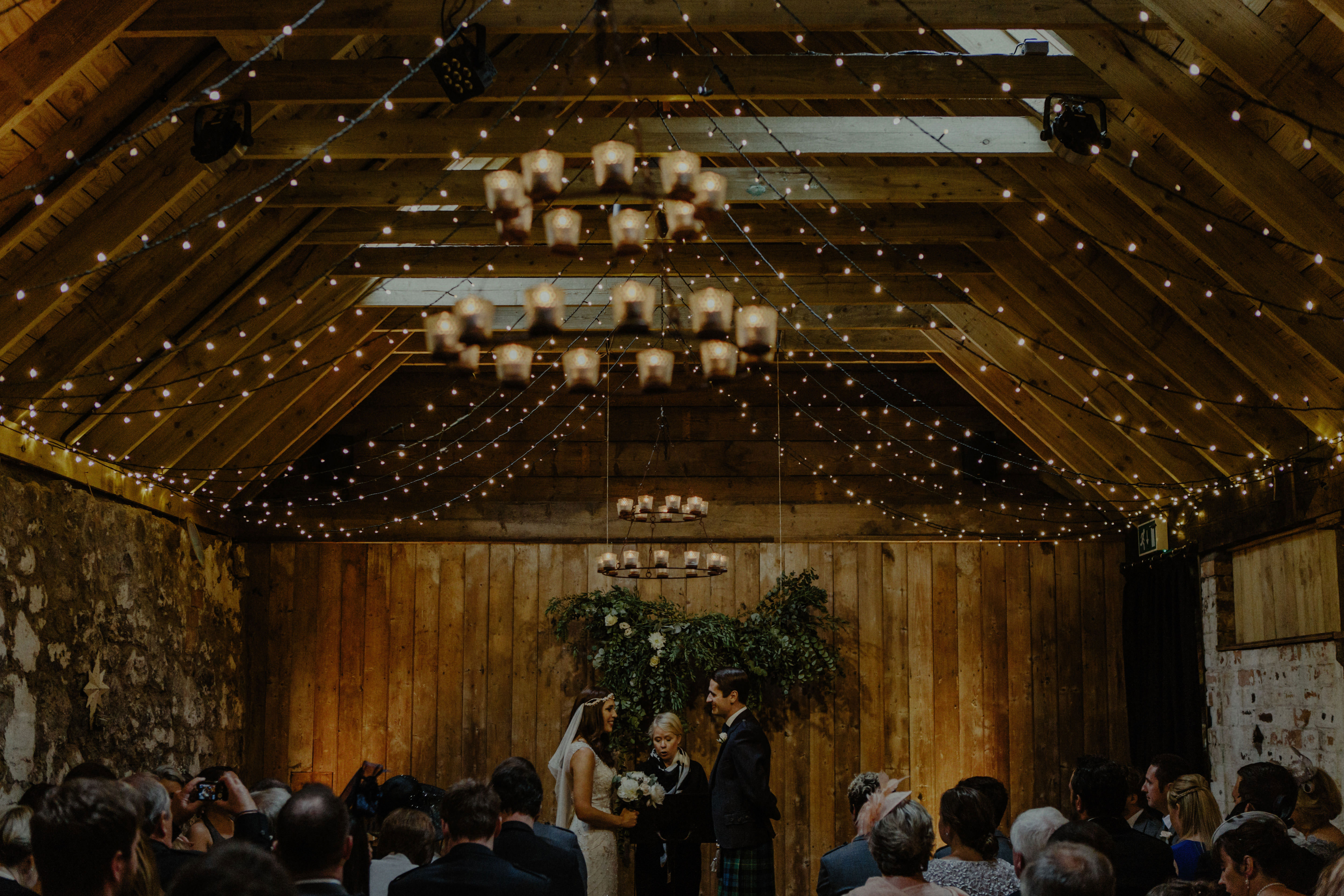 bride and groom stand in front of celebrant during an indoor wedding in ceremony room with wooden beams at byre at inchyra