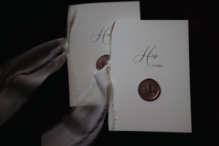 two pieces of card with wax seals and white ribbon with 'His vows' and 'Her vows' written on them 