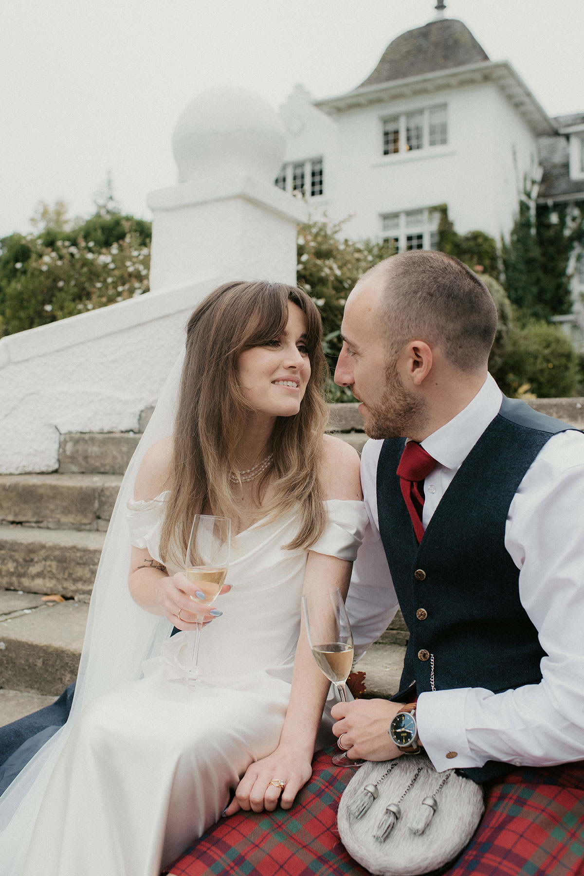 a bride and groom sitting on stone steps outside Achnagairn Castle in Inverness