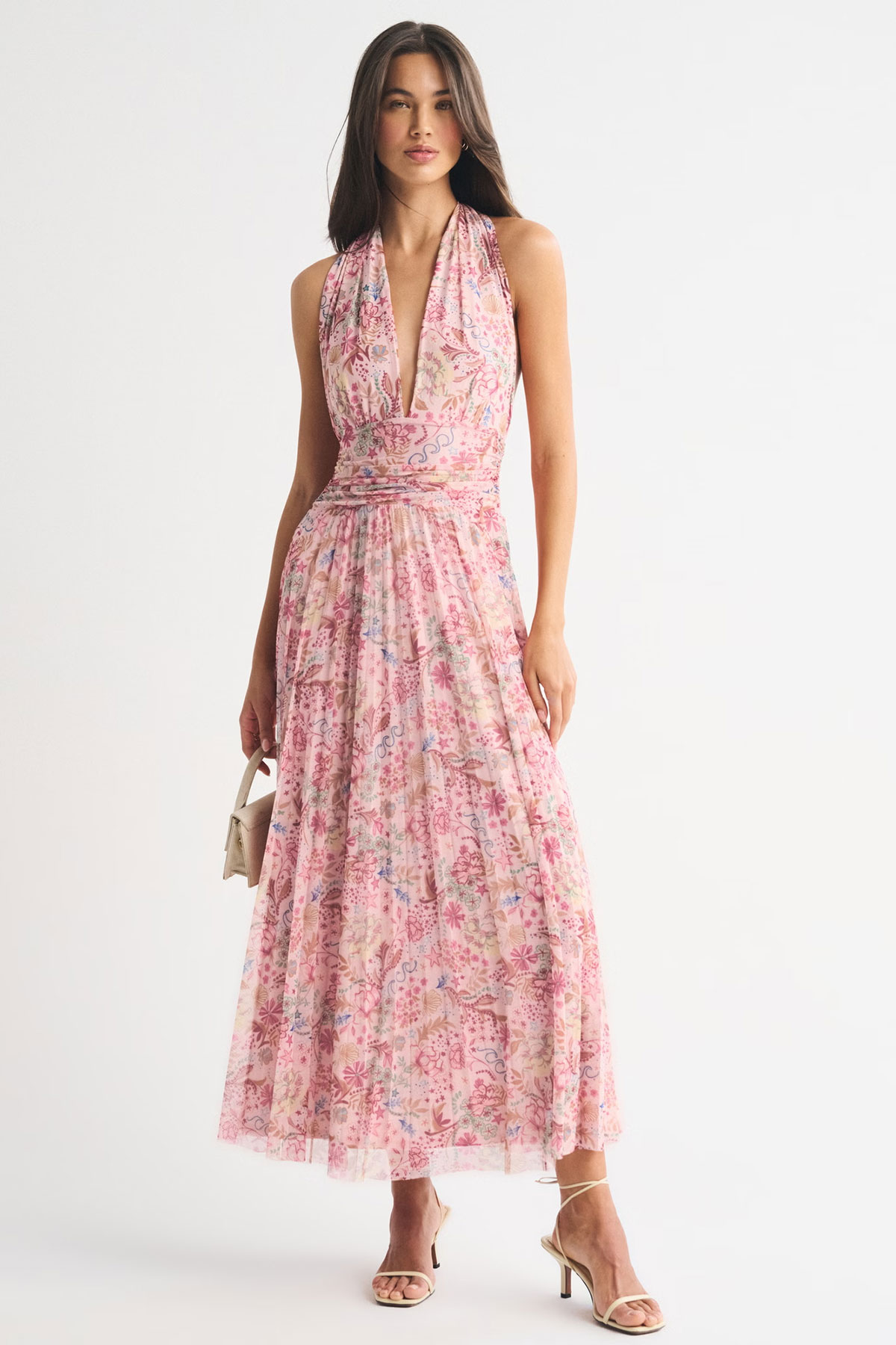 Pink floral halterneck maxi dress with plunging neckline and pleated skirt styled with heels and clutch in a studio setting