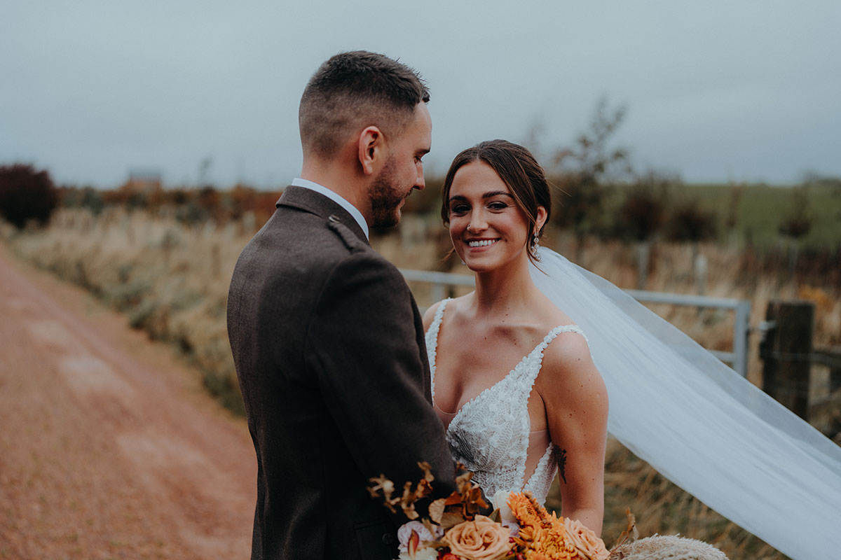 Bride smiling at the camera while groom looks at her