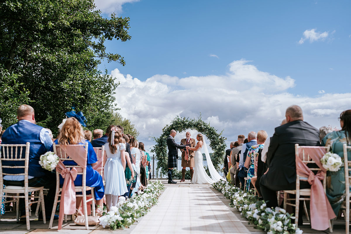 Outdoor wedding ceremony at Lodge on Loch Lomond with floral aisle styling and panoramic loch views