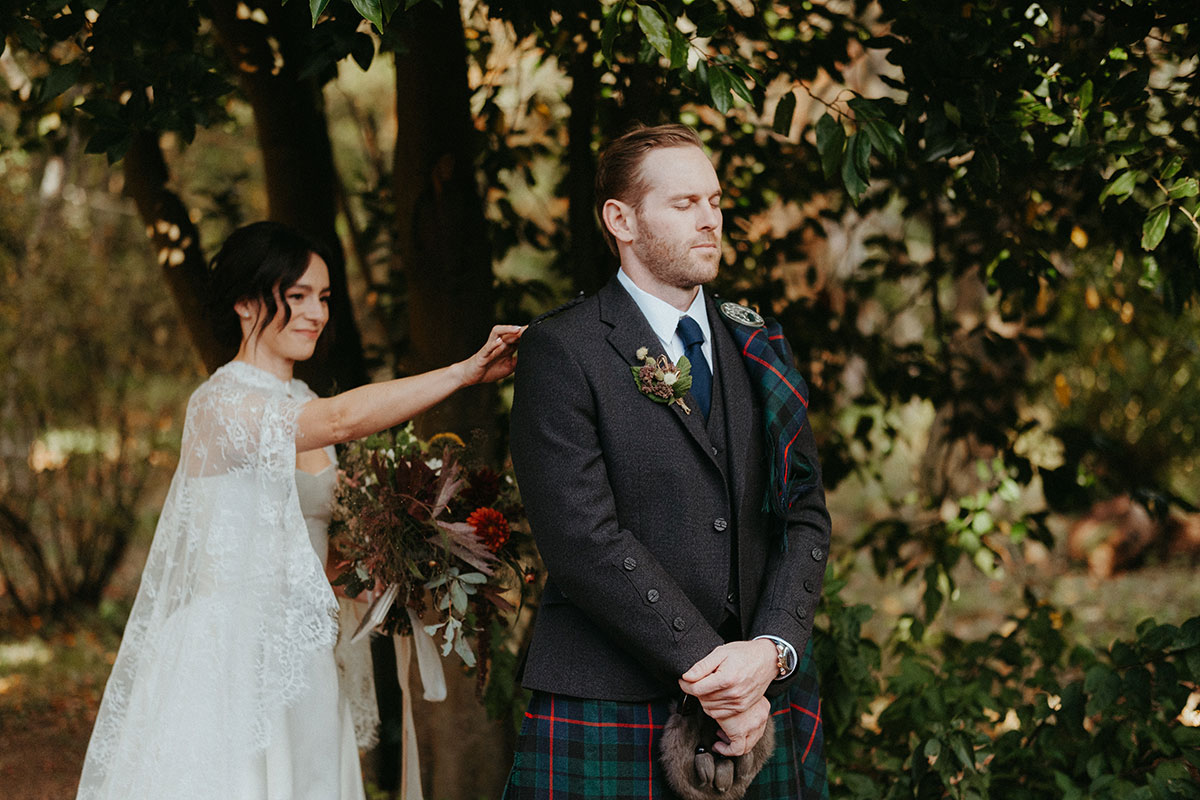 Bride surprising groom during a first look in the gardens at Cambo House, with the groom wearing a kilt and tartan sash.