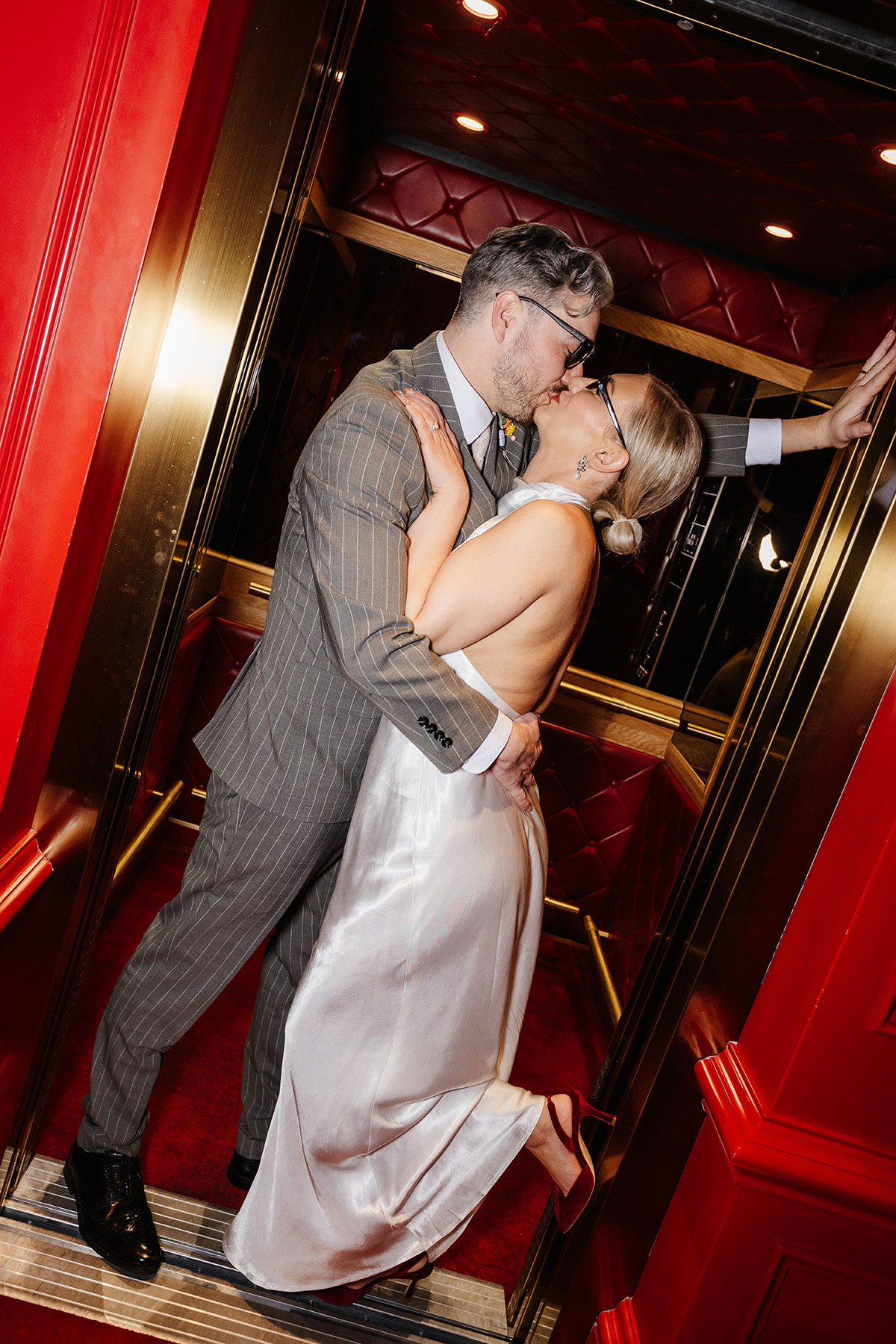 Bride and groom share a romantic kiss inside a red and gold lift at Virgin Hotels Edinburgh, captured by Steph Nicol Photography.