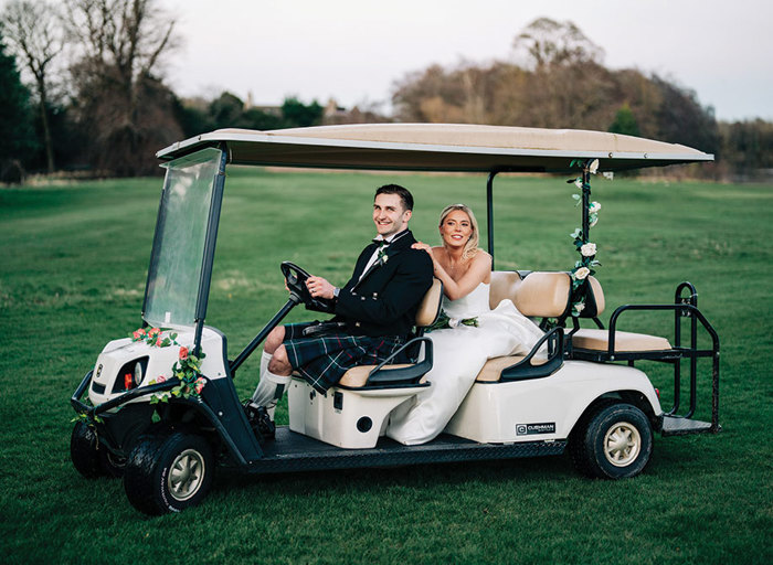 a bride and groom on a golf buggy on a green lawn