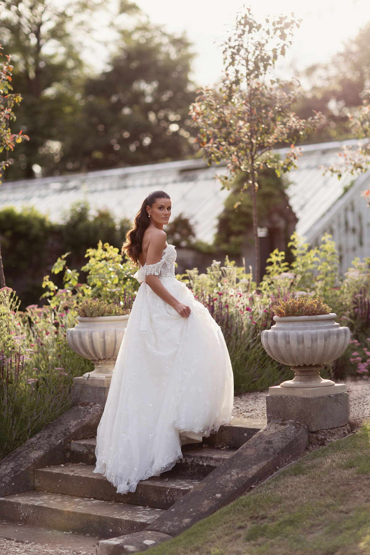 Bride posing in a flower-filled garden during golden hour, with warm sunlight illuminating her wedding dress.