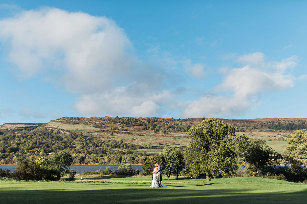 bride and groom hug on wedding day at mar hall with scottish hills and landscape in the background