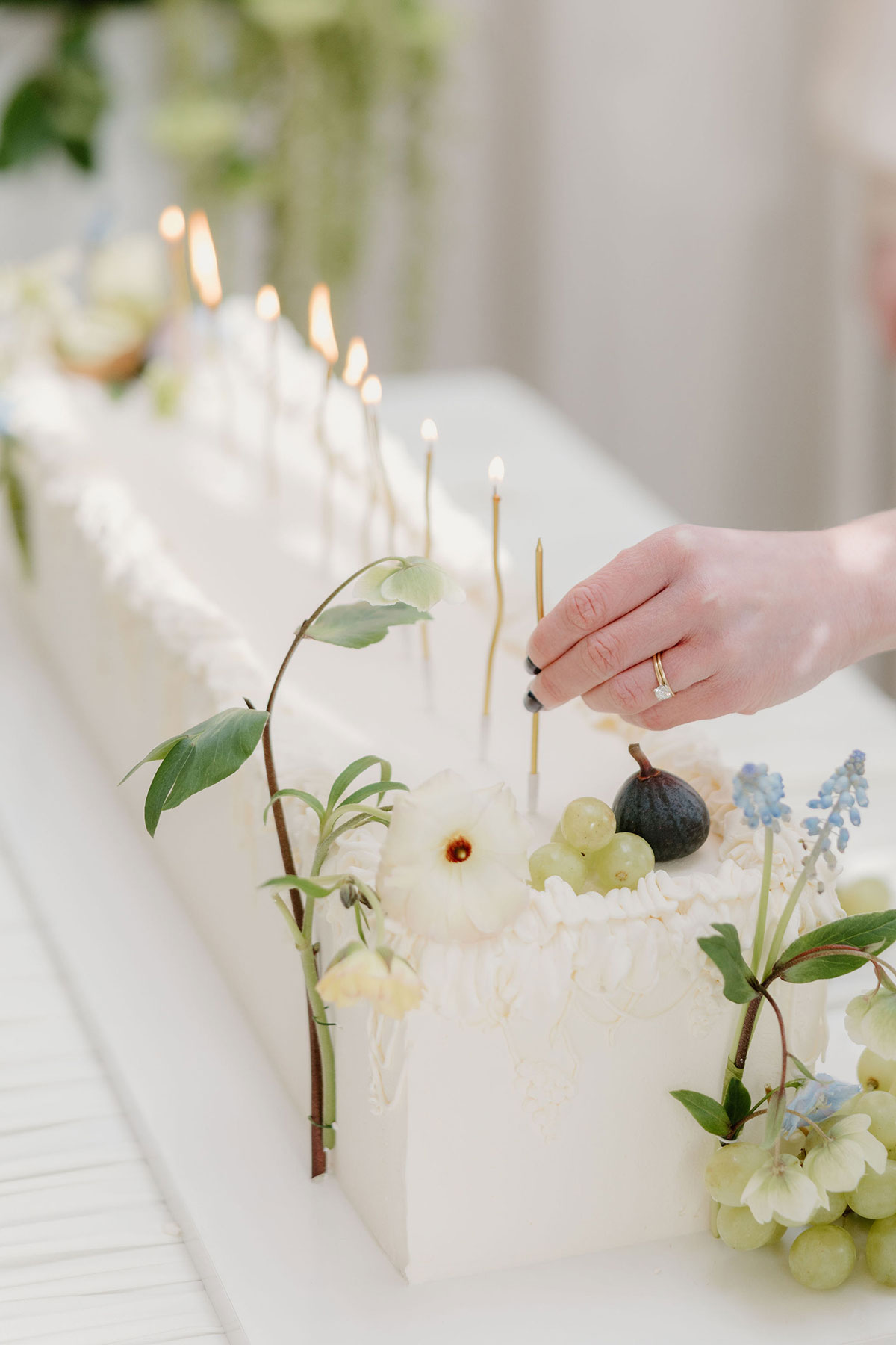 Hand lighting slender candles on a flower-adorned wedding cake