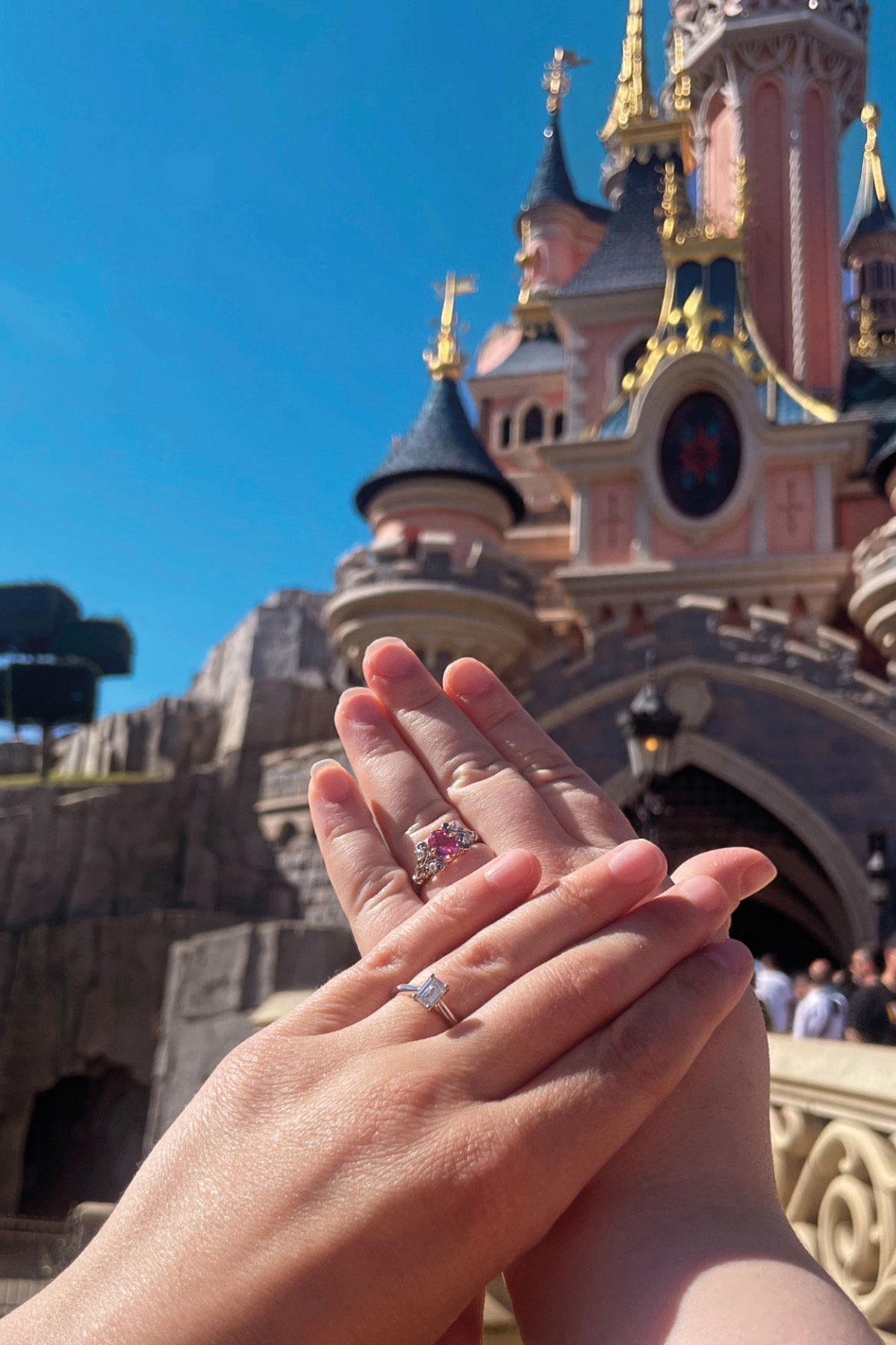 Katie and Mel displaying their engagement rings in front of the castle at Disneyland Paris
