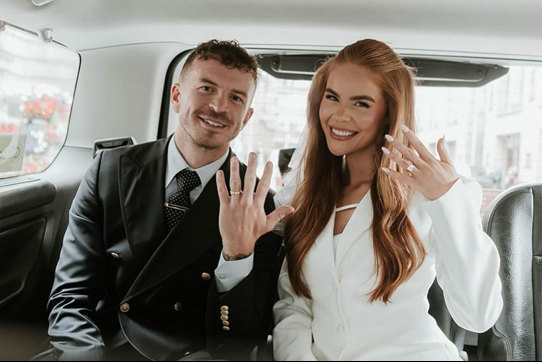 Man and woman sitting in a taxi holding their hands up to show off their wedding rings