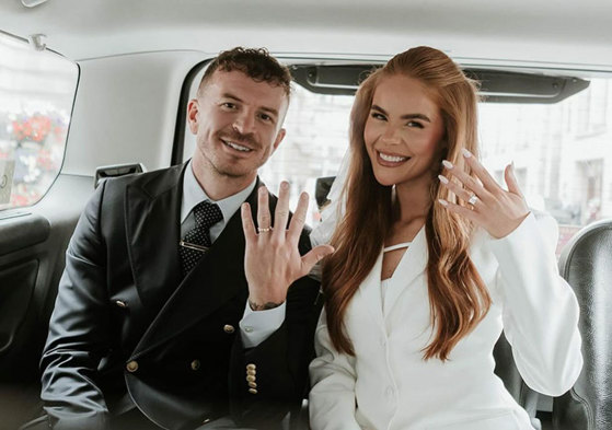 Man and woman sitting in a taxi holding their hands up to show off their wedding rings