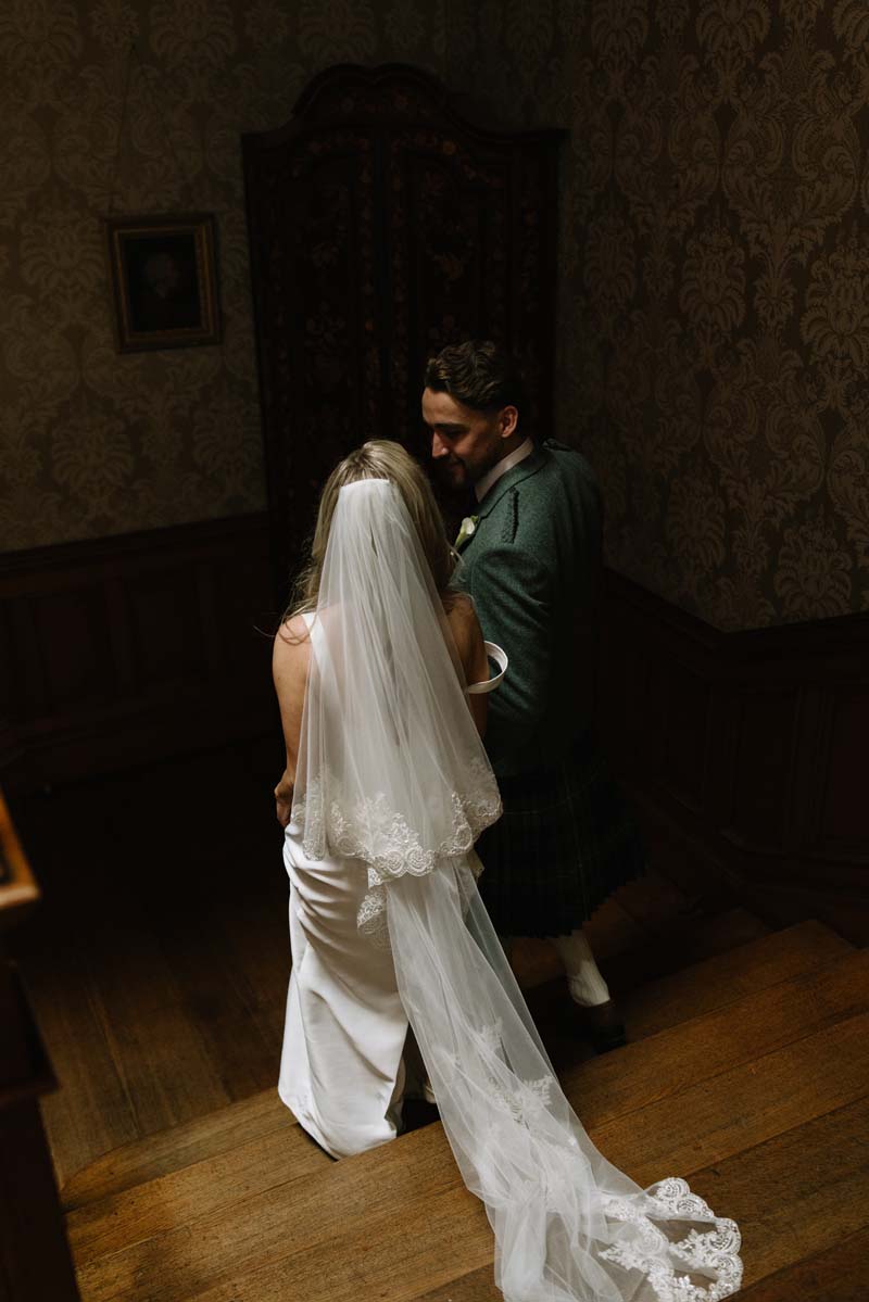 Newlyweds Lia and Louis pose together on the staircase inside Cambo House following their wedding ceremony.
