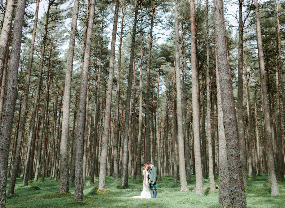 Couple in wedding outfits standing amongst tall trees in forest setting