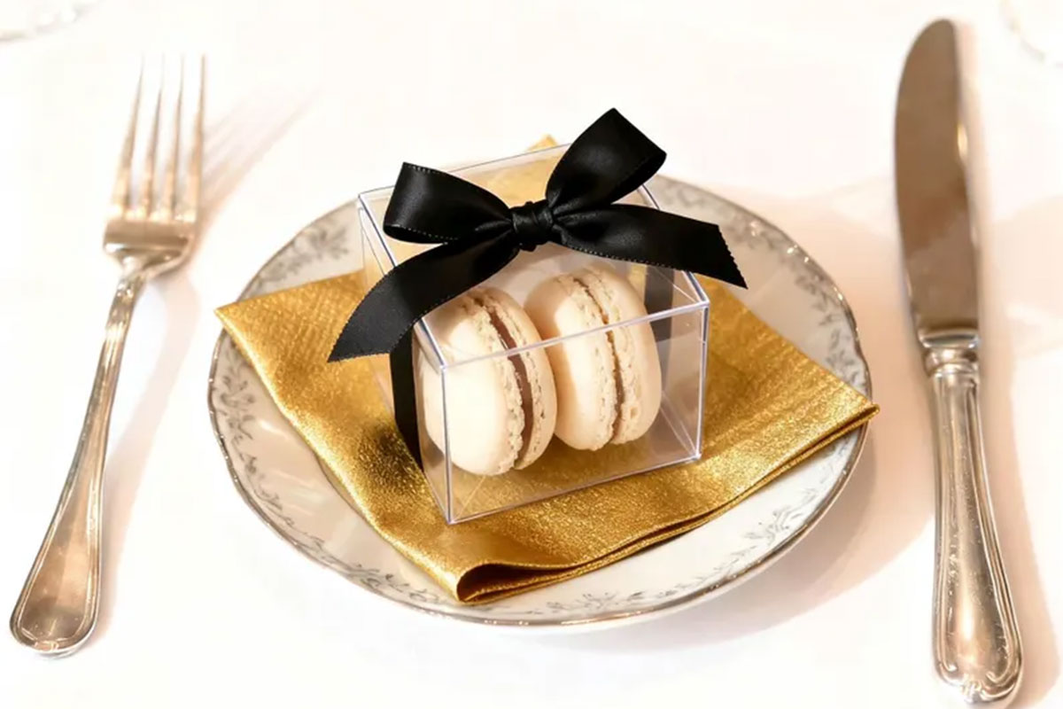 Two white macarons in a clear box with a black bow on a plate at a wedding reception