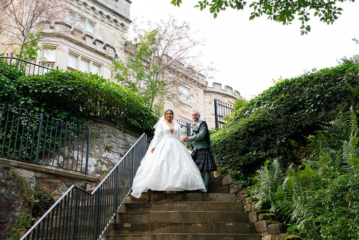 a bride and groom posing on a set of stairs outside a castle.