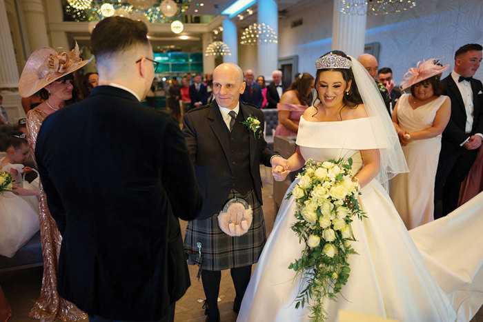 a man in a kilt holding hands with a person in a wedding dress.