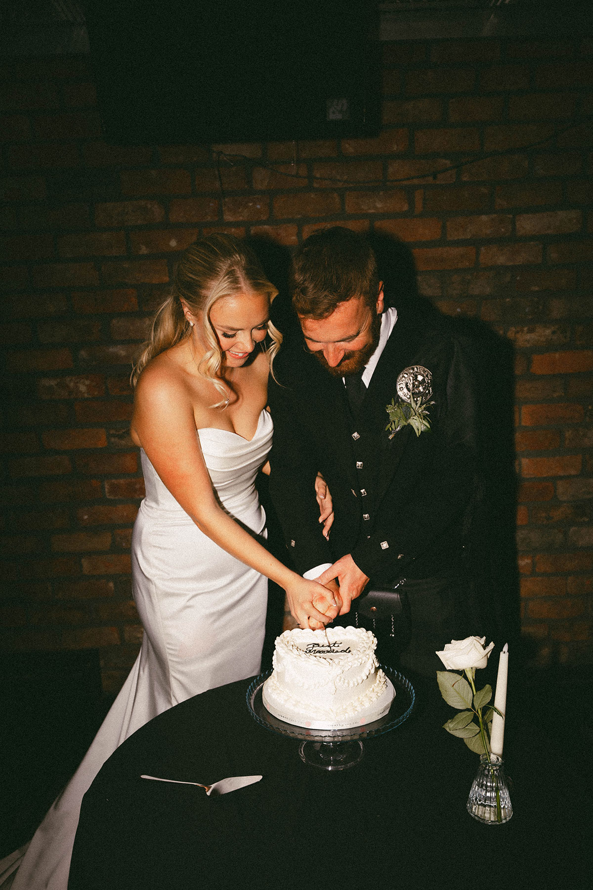 bride and groom cutting just married wedding cake with candle and rose on table