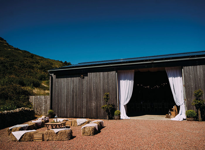 the exterior view of an open barn with curtains pulled aside and hay seating just outside