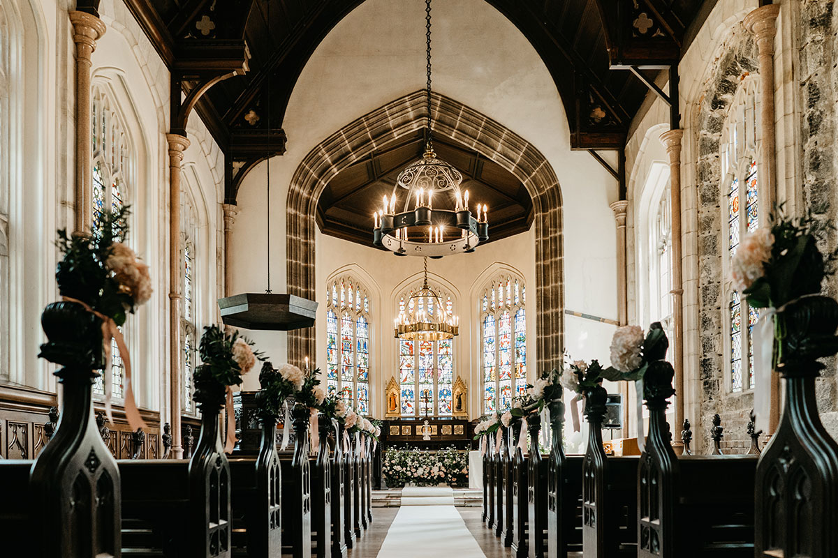 Chapel wedding ceremony space at Cluny Castle with stained-glass windows, floral aisle décor and historic Gothic architecture