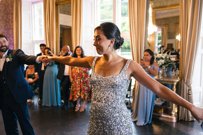 a bride wearing a silver sequin dress holds her arms wide while dancing with the groom during a wedding reception at Blairquhan Castle